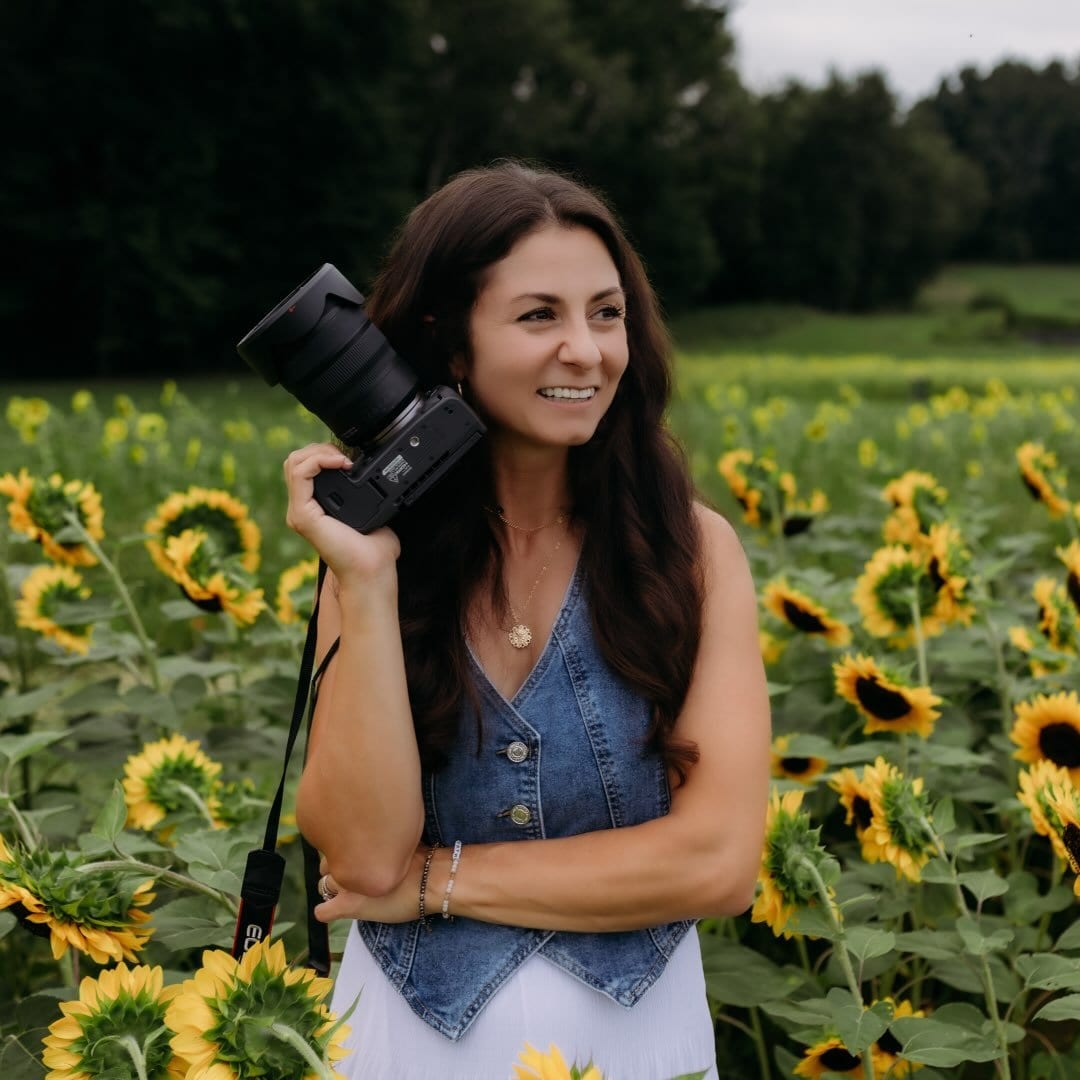 Nicole, lead photographer of Hometown Media Lifestyle, holding her camera in a sunflower field